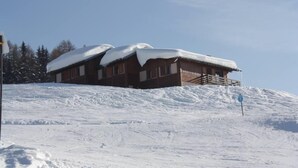 Een houten lodge met een met sneeuw bedekte kap, gelegen op een besneeuwde helling.