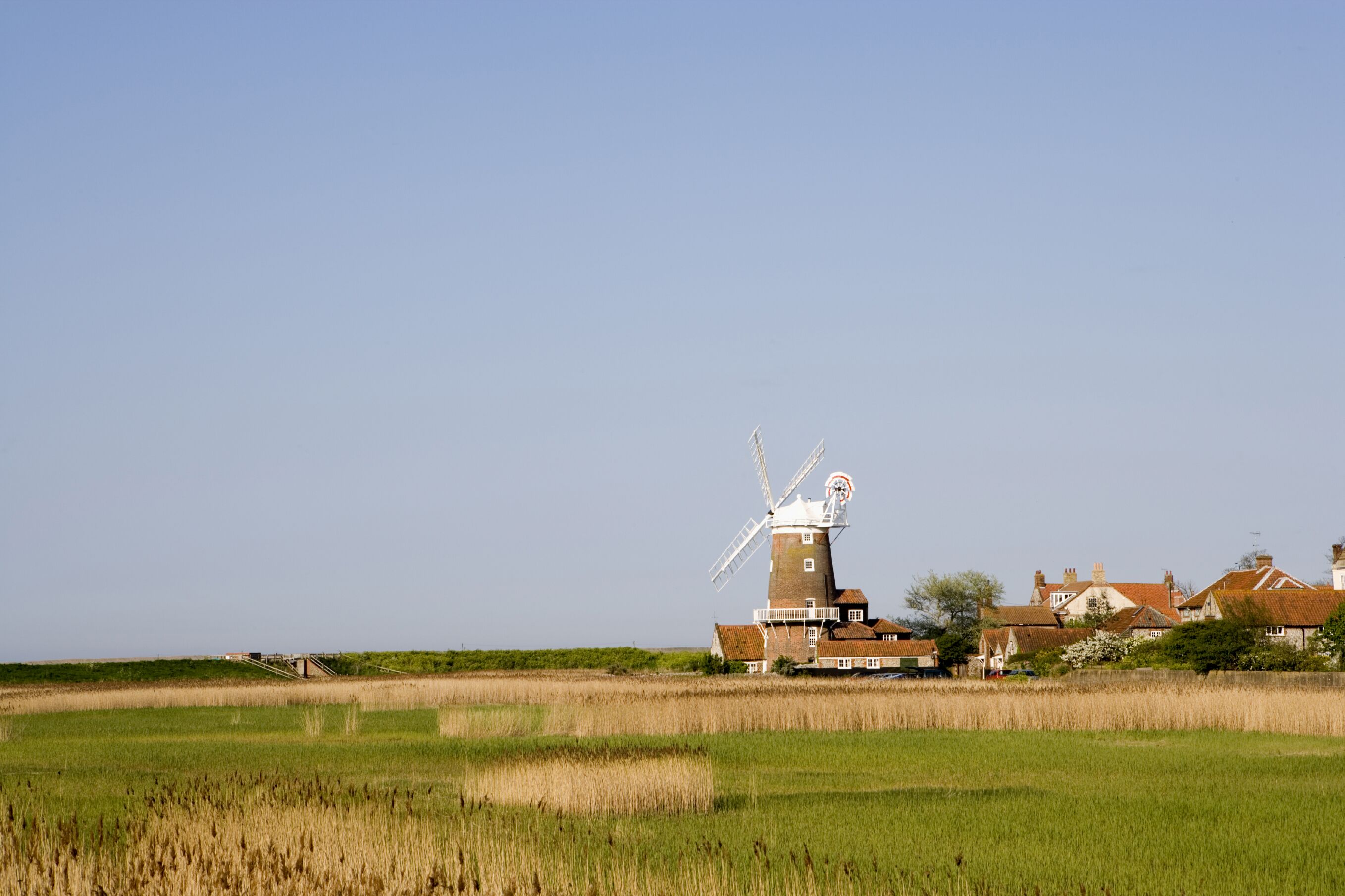 A traditional windmill in a rural setting with surrounding houses and fields.
