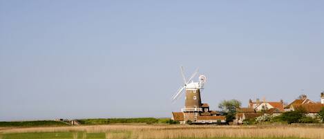A traditional windmill in a rural setting with surrounding houses and fields.