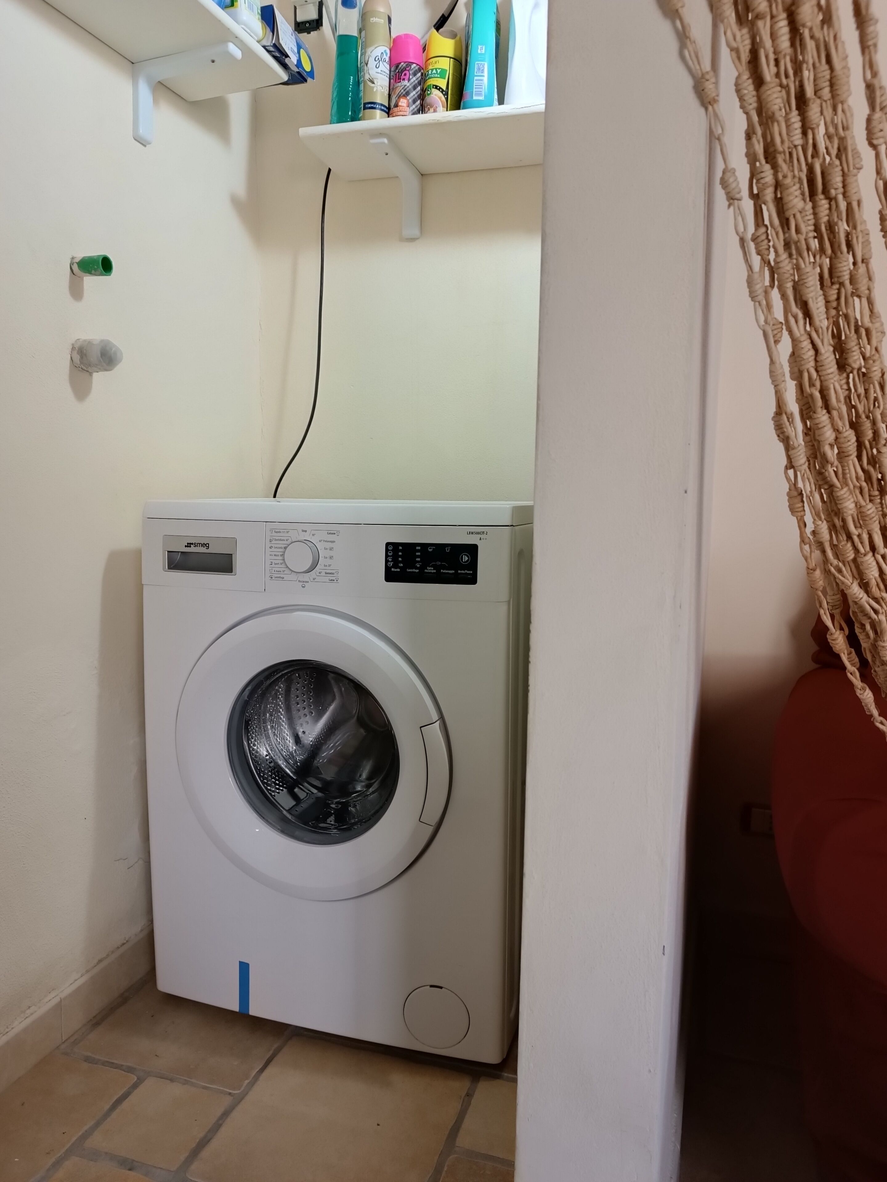 A compact, white washing machine in a small laundry room with a tiled floor.