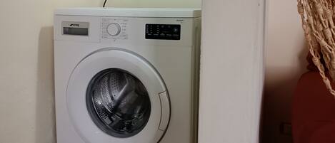A compact, white washing machine in a small laundry room with a tiled floor.