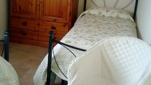 A bedroom with a wooden wardrobe, a bed with a floral bedspread, and a white quilted chair.
