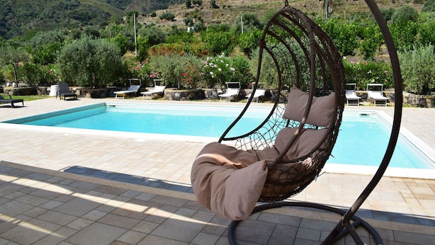 A poolside area with a hanging chair, lounge chairs, and a view of a mountainous landscape.