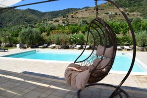 Zona de piscina con una hamaca colgante, sillas de descanso y vistas a un paisaje montañoso.