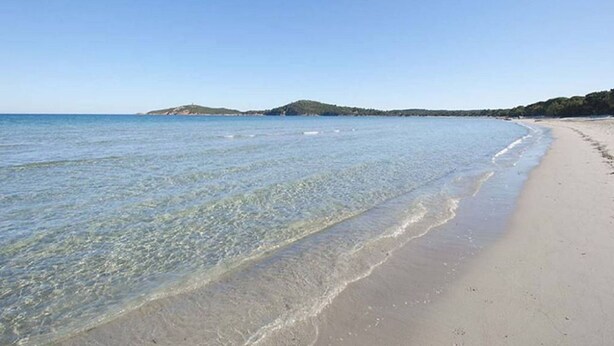 A beach with clear shallow waters, a sandy shore, and distant hills.