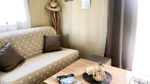 A cozy room with a patterned sofa, a small wooden table with a book and a candle, and a wall with a hat and two framed pictures.