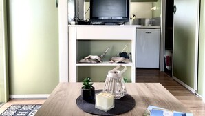 A compact living space with a kitchenette, a television, a small refrigerator, and a dining area with a table set for two.
