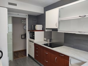 A modern kitchen with white cabinets, a microwave, an oven, and a black induction cooktop.