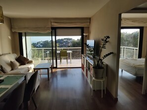 A room with a balcony, a sofa, a dining table, a TV, and a potted plant.