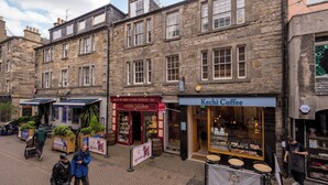 Un edificio histórico de piedra con varias fachadas comerciales, incluyendo una cafetería y una tienda que vende entradas para conciertos.