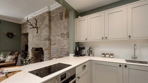 Una cocina con armarios blancos, una pared de piedra, horno empotrado y cafetera.