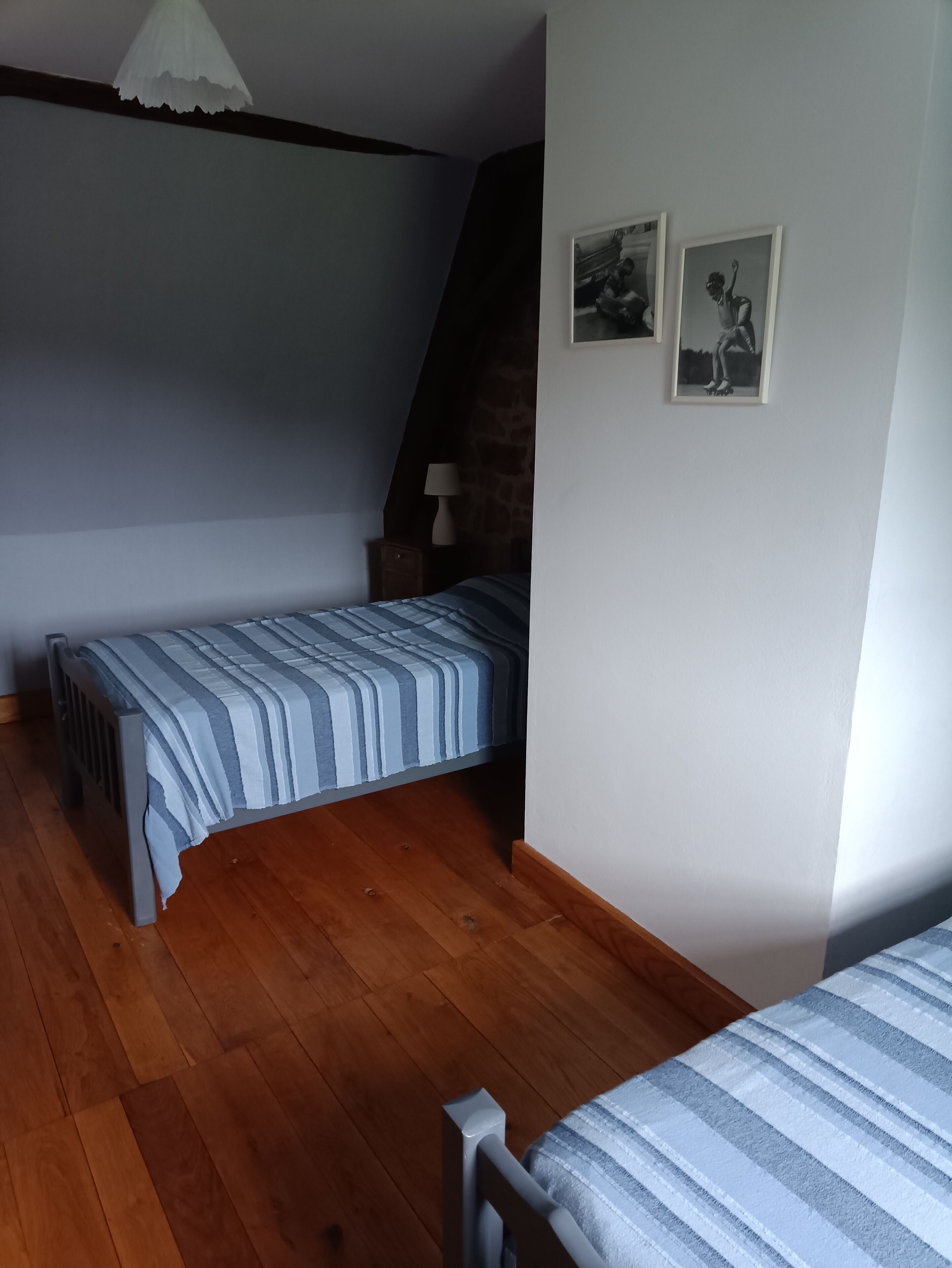 Une chambre à coucher avec un lit, une table de chevet, une lampe et deux tableaux encadrés accrochés au mur.