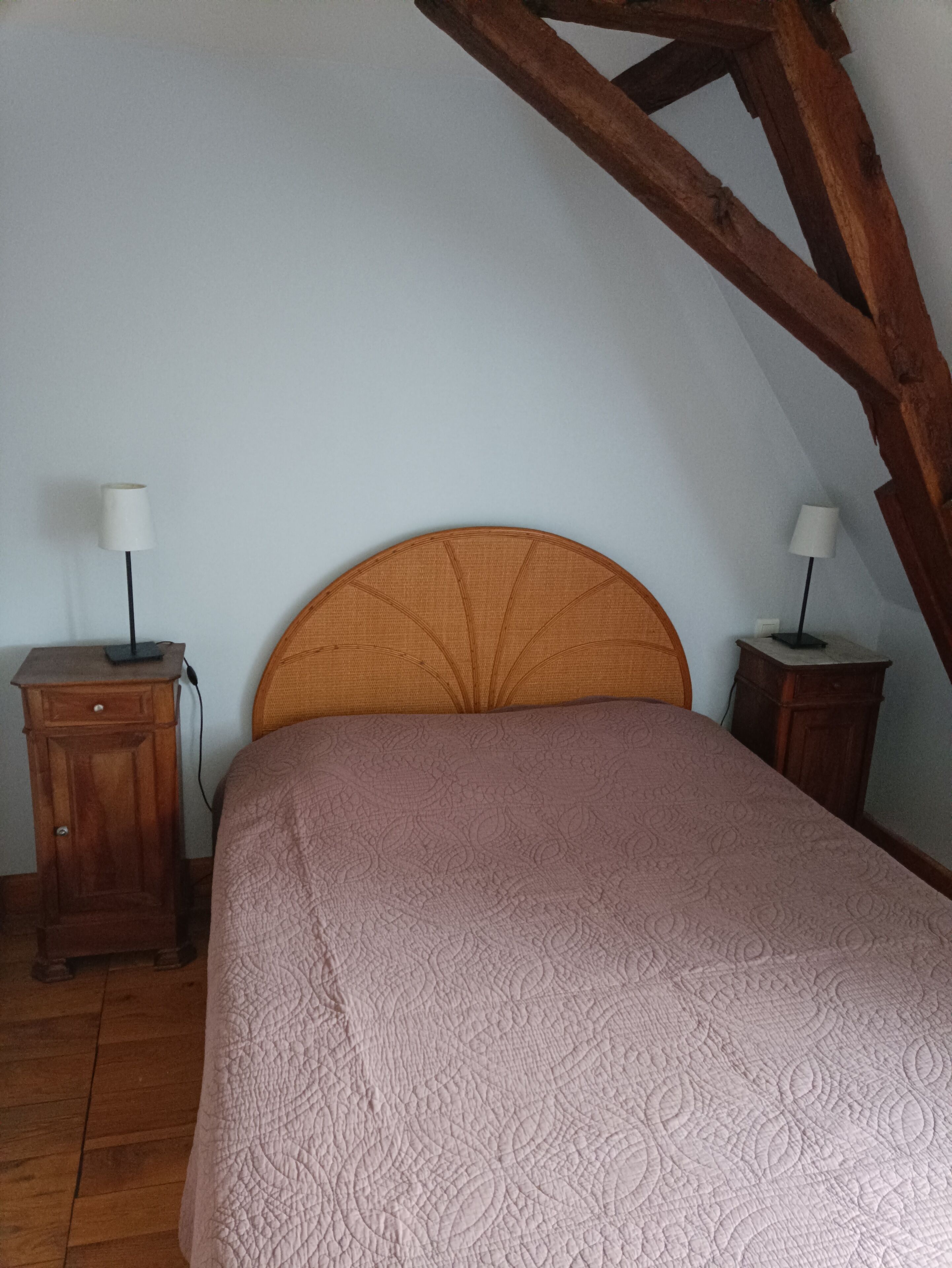 Une chambre à coucher avec une tête de lit en bois, un lit recouvert d’une couvre-lit à motifs, deux tables de chevet avec des lampes et un plancher en bois.