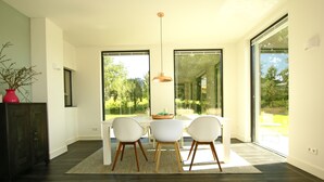 A dining area with a white table and chairs, a hanging pendant light, and large windows offering a view of greenery. - The ground floor of a beautifully renovated luxury farm! (Erlecom)