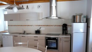 A modern kitchen with a dishwasher, oven, refrigerator, and a dining table with chairs. - In Marignac, house of 70m2, all comfort, with closed courtyard. (5 people) (Marignac)
