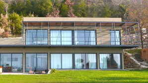 Une maison moderne à deux étages, dotée de grandes fenêtres, d’un toit plat et d’un mur de soutènement en pierre.