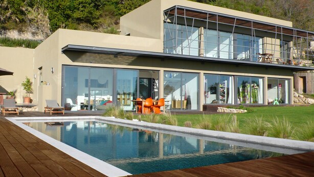 Une maison moderne dotée d’une piscine, de grandes baies vitrées et d’une terrasse aménagée avec du mobilier d’extérieur.
