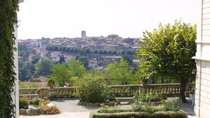 Une cour donnant sur la ville, un jardin fleuri et un banc.