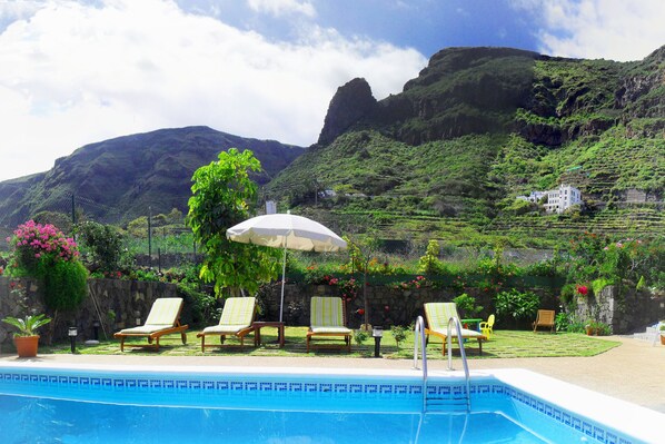 A pool area with lounge chairs and an umbrella, surrounded by lush greenery and mountains. - HOLIDAY HOME "EL MAR" - Nice villa with swimming pool & garden (San Juan de la Rambla)