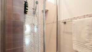 Une douche fermée par des parois en verre, dotée d’un pommeau de douche à main et d’un robinet mural.