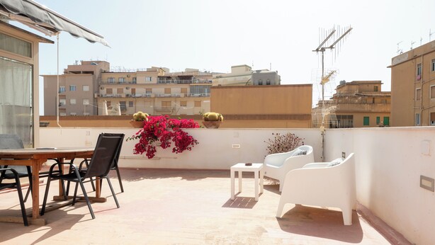 Une terrasse sur le toit, avec une table et des chaises, des plantes en pot et une vue sur les bâtiments environnants.