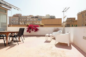 Eine Dachterrasse mit Tisch und Stühlen, Blumentöpfen und Blick auf die umliegenden Gebäude.