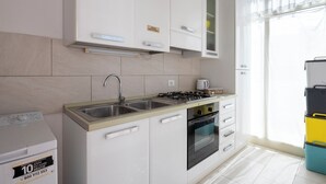 Une cuisine moderne avec des armoires blanches, un évier en acier inoxydable, une cuisinière à gaz et un four encastré.