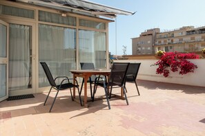 Ein Balkon mit Tisch und Stühlen, eine Schiebetür und rote Blumen an der Wand.