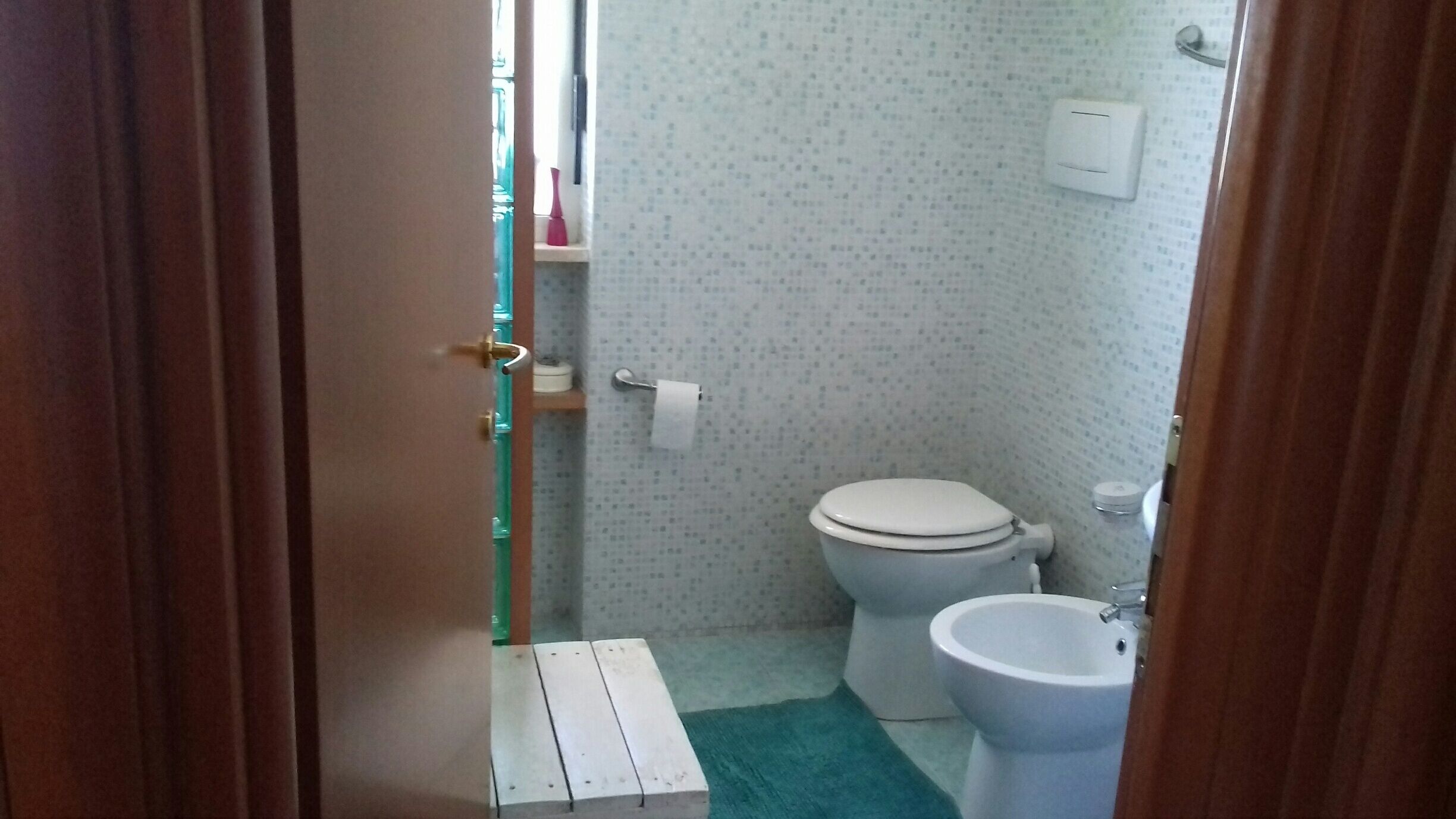 Un baño pequeño con inodoro, bidé y un escalón de madera que conduce a la zona de la ducha.