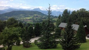 Een landelijk landschap met een huis, omgeven door bomen en een uitzicht op verre bergen.