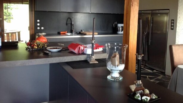 Een moderne keuken met donkere kastjes, een roestvrijstalen koelkast en een eethoek met een tafel gedekt voor twee personen.