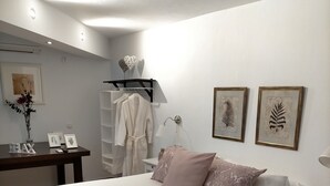 Un dormitorio con una cama, una mesita de noche, un perchero para bata y dos cuadros con motivos de hojas en la pared.