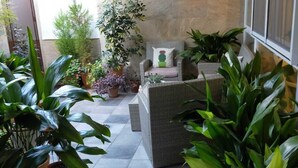Un patio cubierto con un muro de piedra, un sofá de mimbre y varias macetas con plantas.