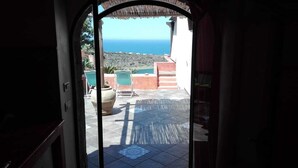 A view from a doorway to an outdoor patio with a tiled floor, a large pot, and green chairs. - RESIDENCE VENUS DREAM (Pantelleria)
