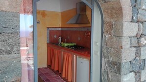 A compact kitchen with a red countertop, a built-in stove, and a small refrigerator. - RESIDENCE VENUS DREAM (Pantelleria)