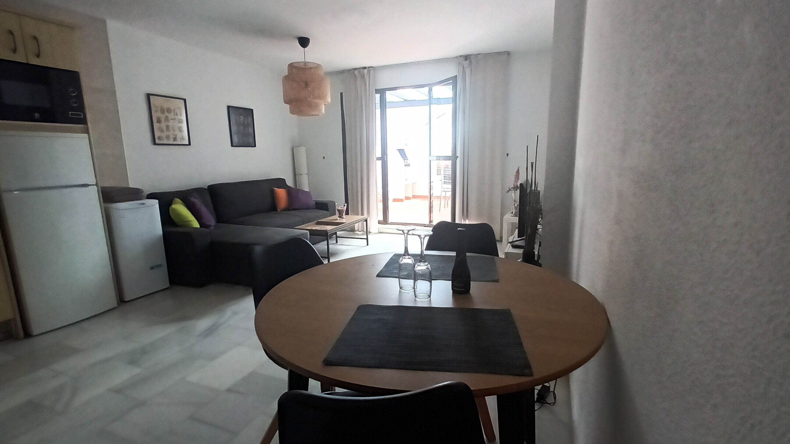 A compact living space with a kitchenette, a sofa, a dining table with chairs, and a large window providing natural light.