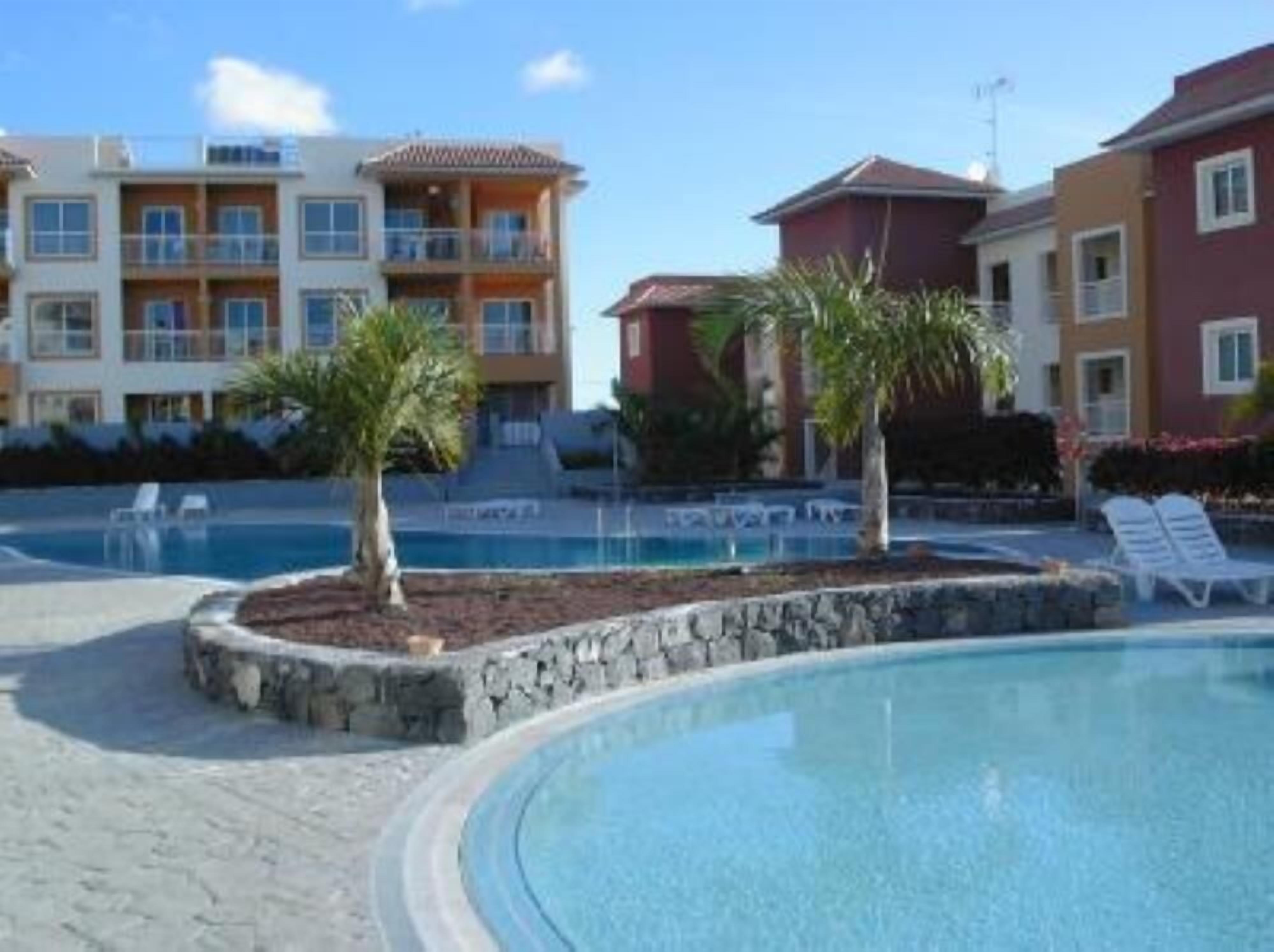 A resort with a swimming pool, palm trees, and multi-story buildings with balconies.