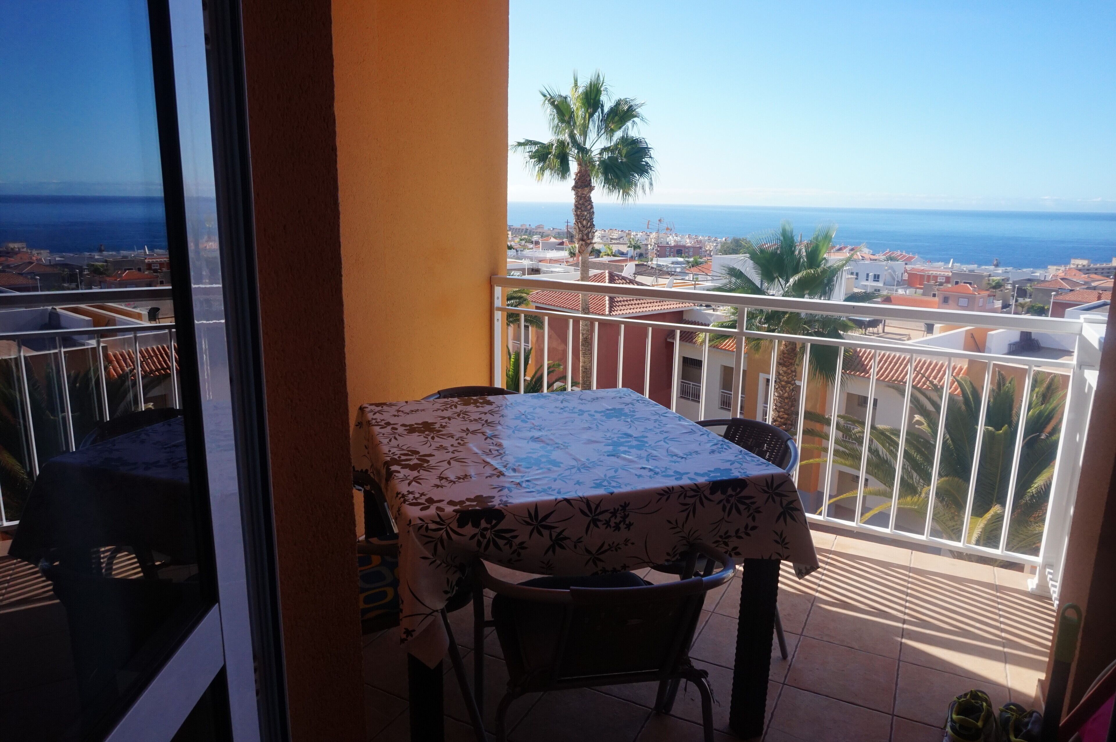 Un balcon avec une table et des chaises, donnant sur une ville côtière et la mer.