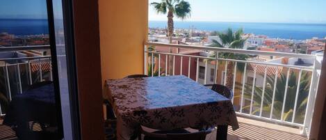 Un balcon avec une table et des chaises, donnant sur une ville côtière et la mer.