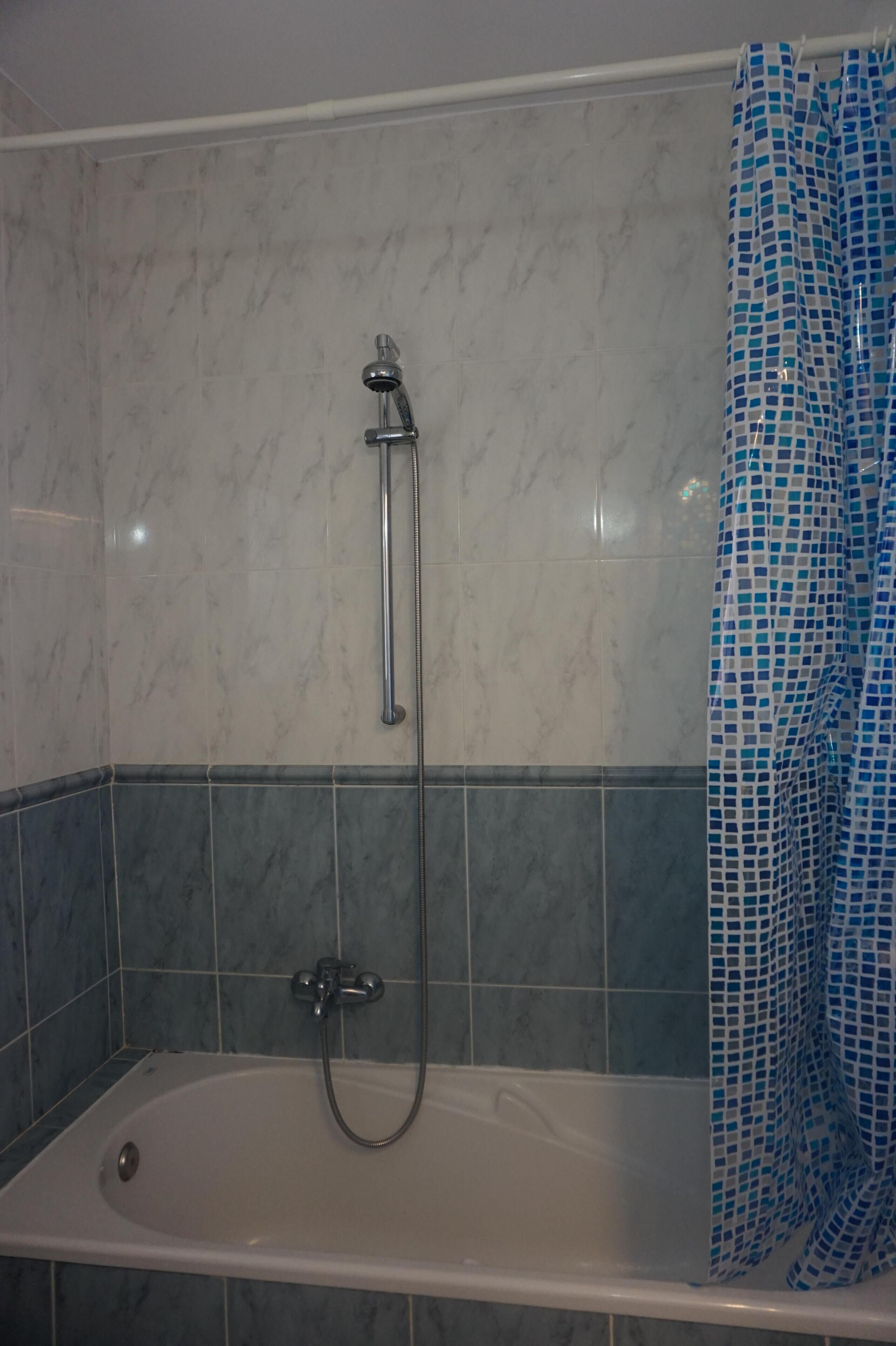 Ein Badezimmer mit Badewanne, Duschkopf und einem blauen, gemusterten Duschvorhang.
