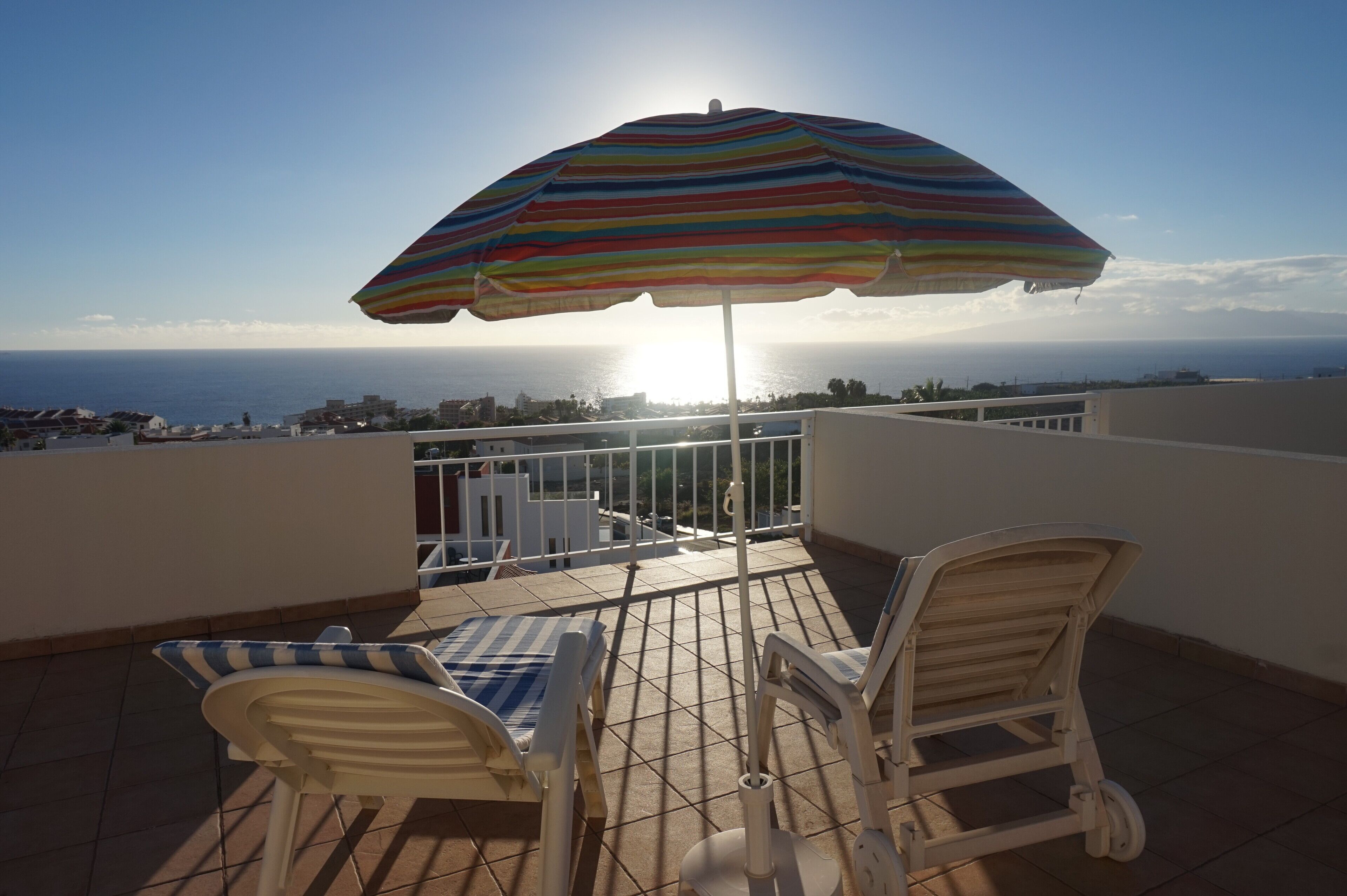 Ein Balkon mit einem gestreiften Sonnenschirm, zwei Liegestühlen und Blick aufs Meer.