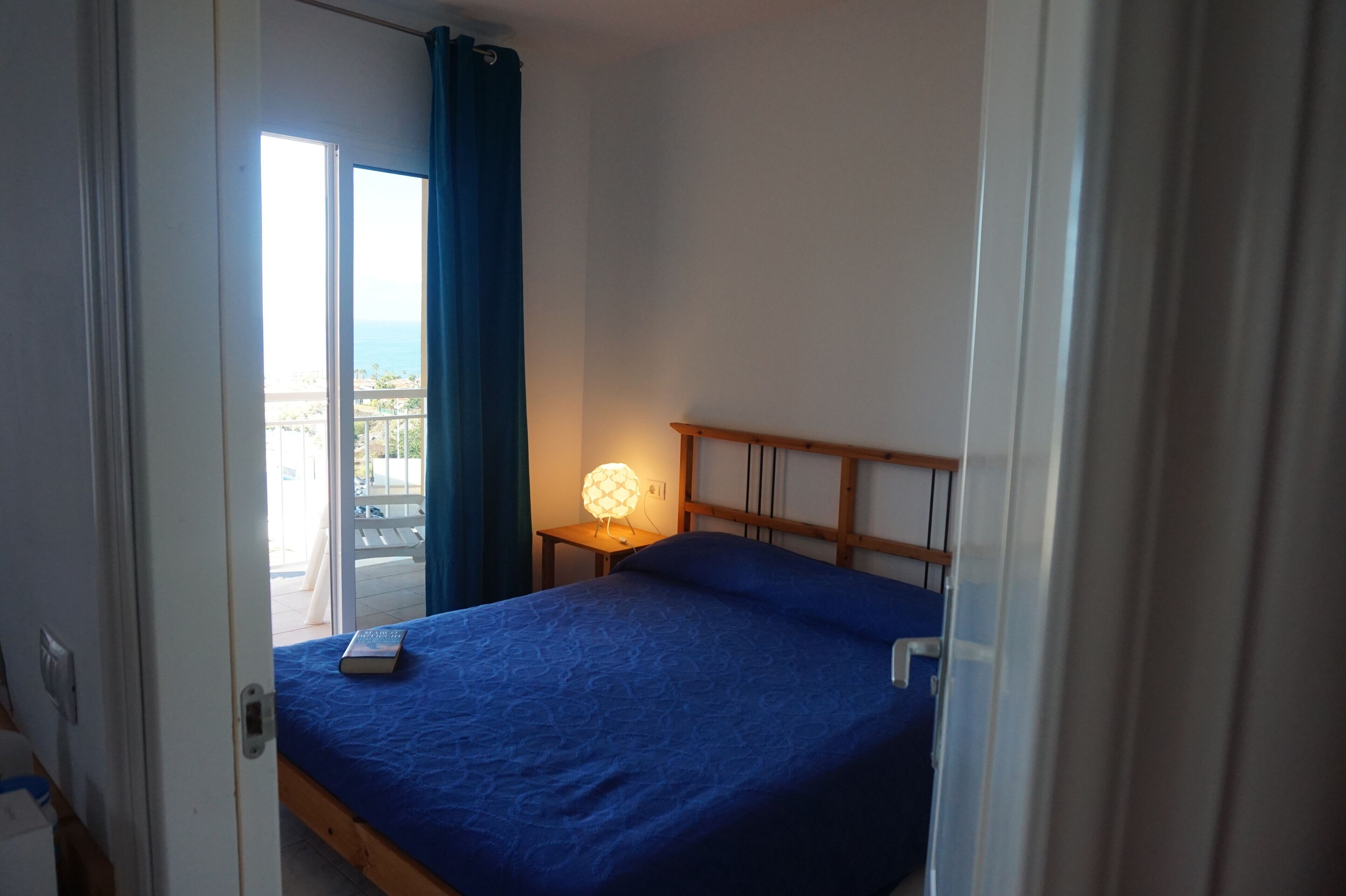 Un dormitorio con cama, una mesita de noche con lámpara y vistas al exterior a través de una puerta corredera.