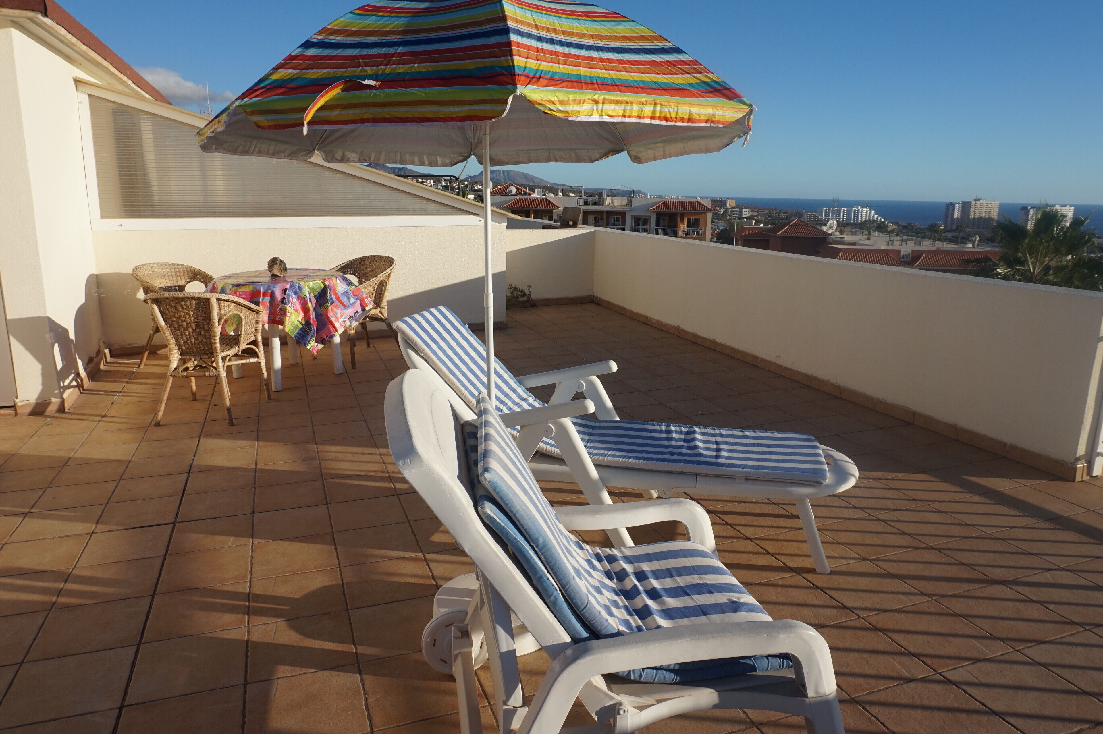 Une terrasse sur le toit, avec des chaises longues, une table et un parasol rayé aux couleurs vives.