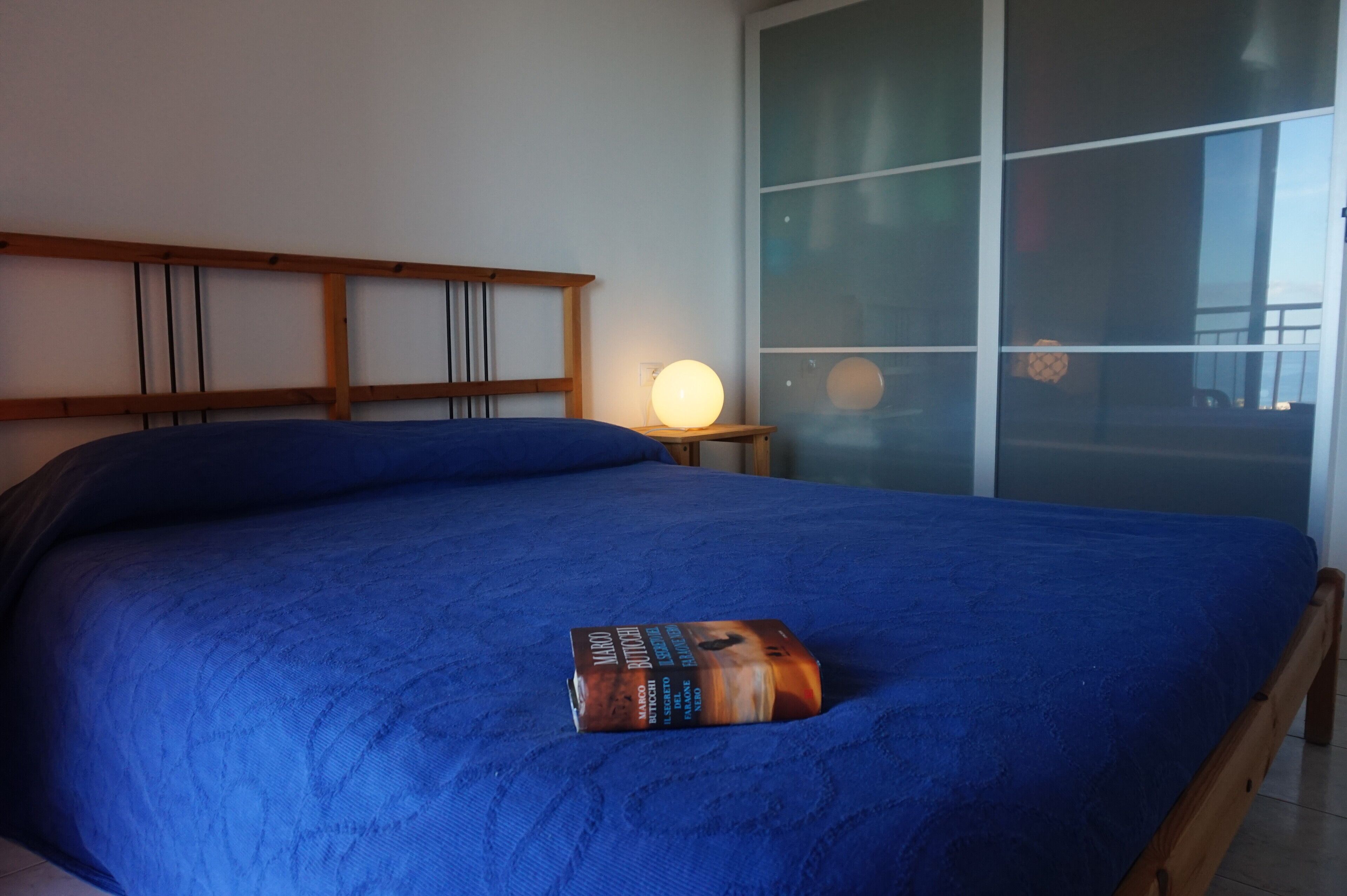 A bed with a blue bedspread and a book titled "Manu" on it.