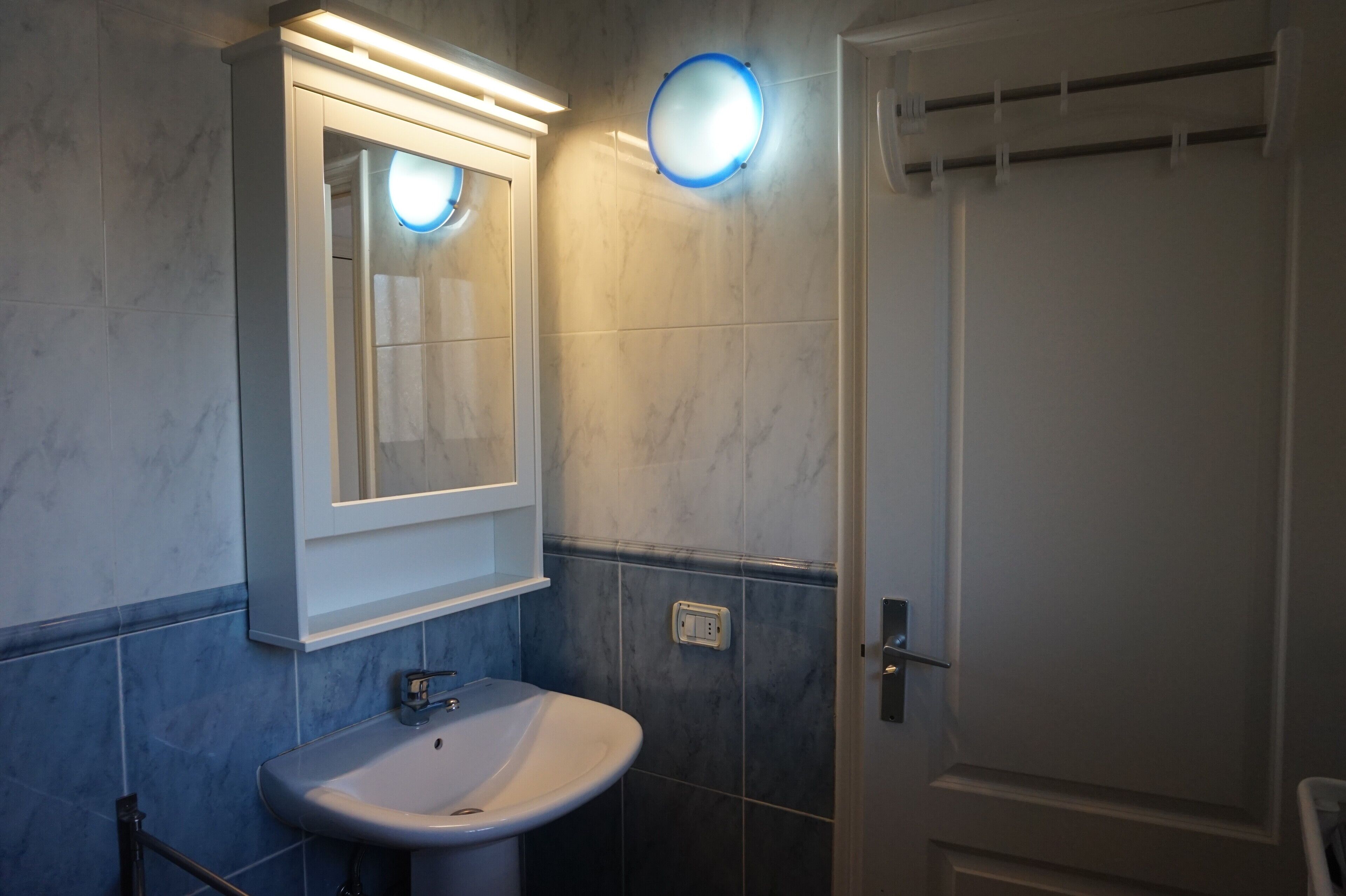 A bathroom with a white sink, a mirror with a light, and a door with a handle.