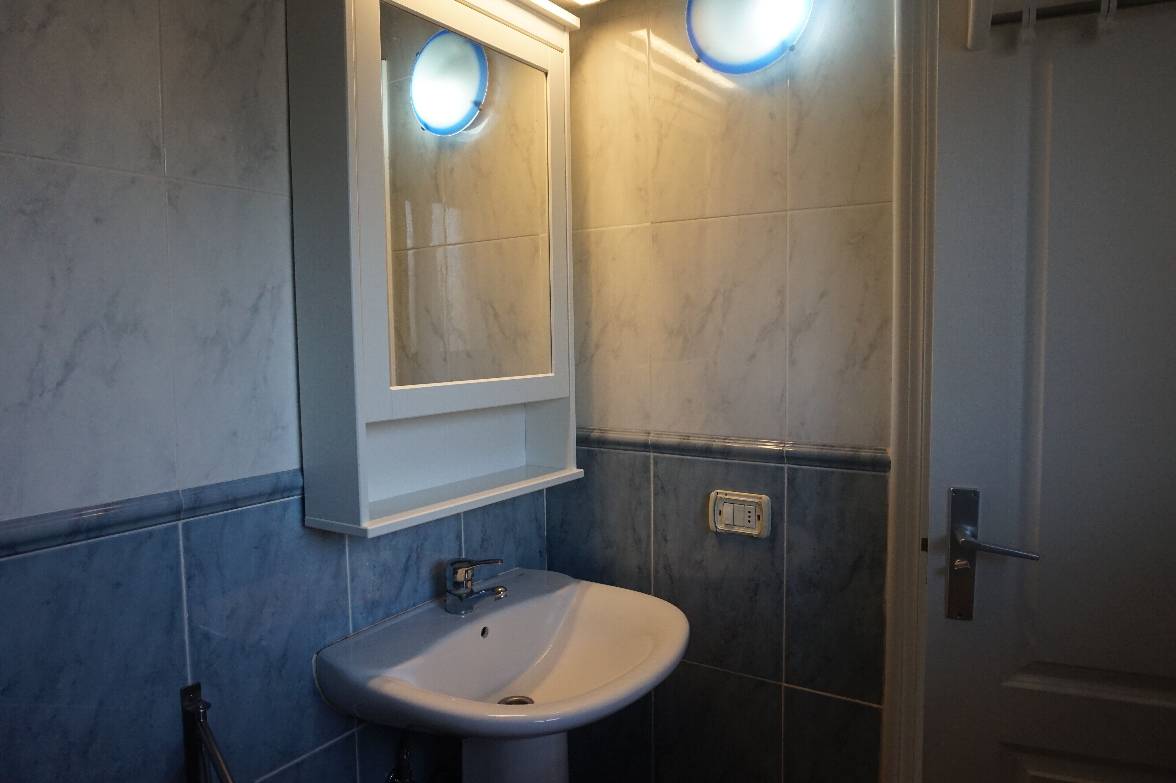 A bathroom with a white sink, a mirror, and a light switch on the wall.