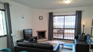 A living room with a fireplace, a television, a sofa, a dining table, and a balcony with a view. - Apartment With Fabulous Sea Views, Excellent Facilities, Heated Indoor Pool (malaga)