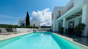 A rectangular swimming pool with clear blue water, surrounded by a white building with a balcony.