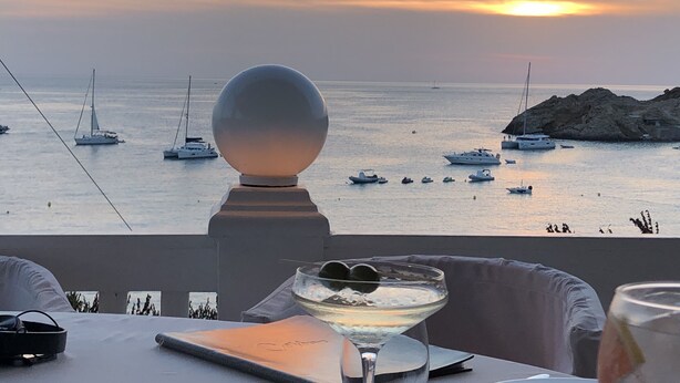 A sunset view from a terrace with a table, chairs, and a decorative sphere.
