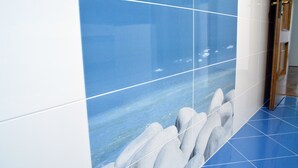 Un pasillo con paredes y piso de azulejos azules, que presenta un gran mural de rocas y agua.